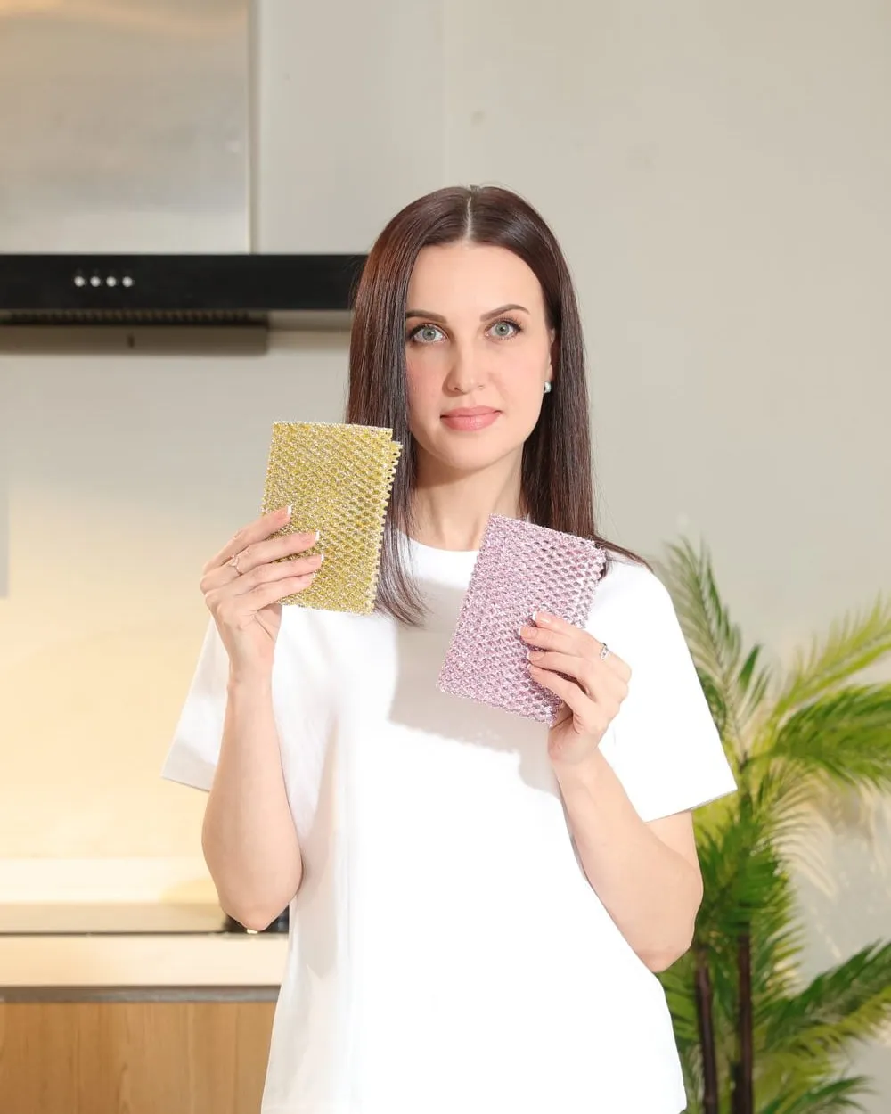 Woman holding golden and pink non-scratch scrubbers, labelled non-scratch, odor-free and long-lasting