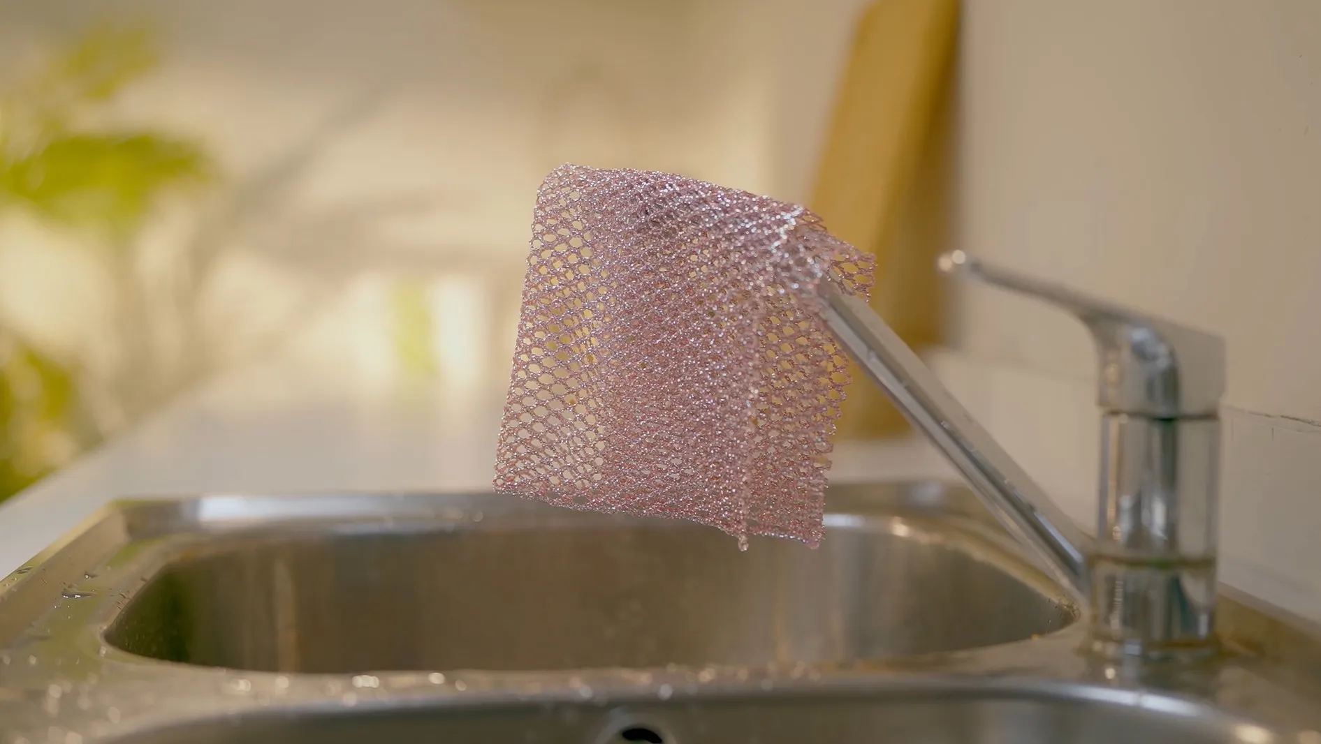 Pink mesh scourer hanging over the sink faucet to dry