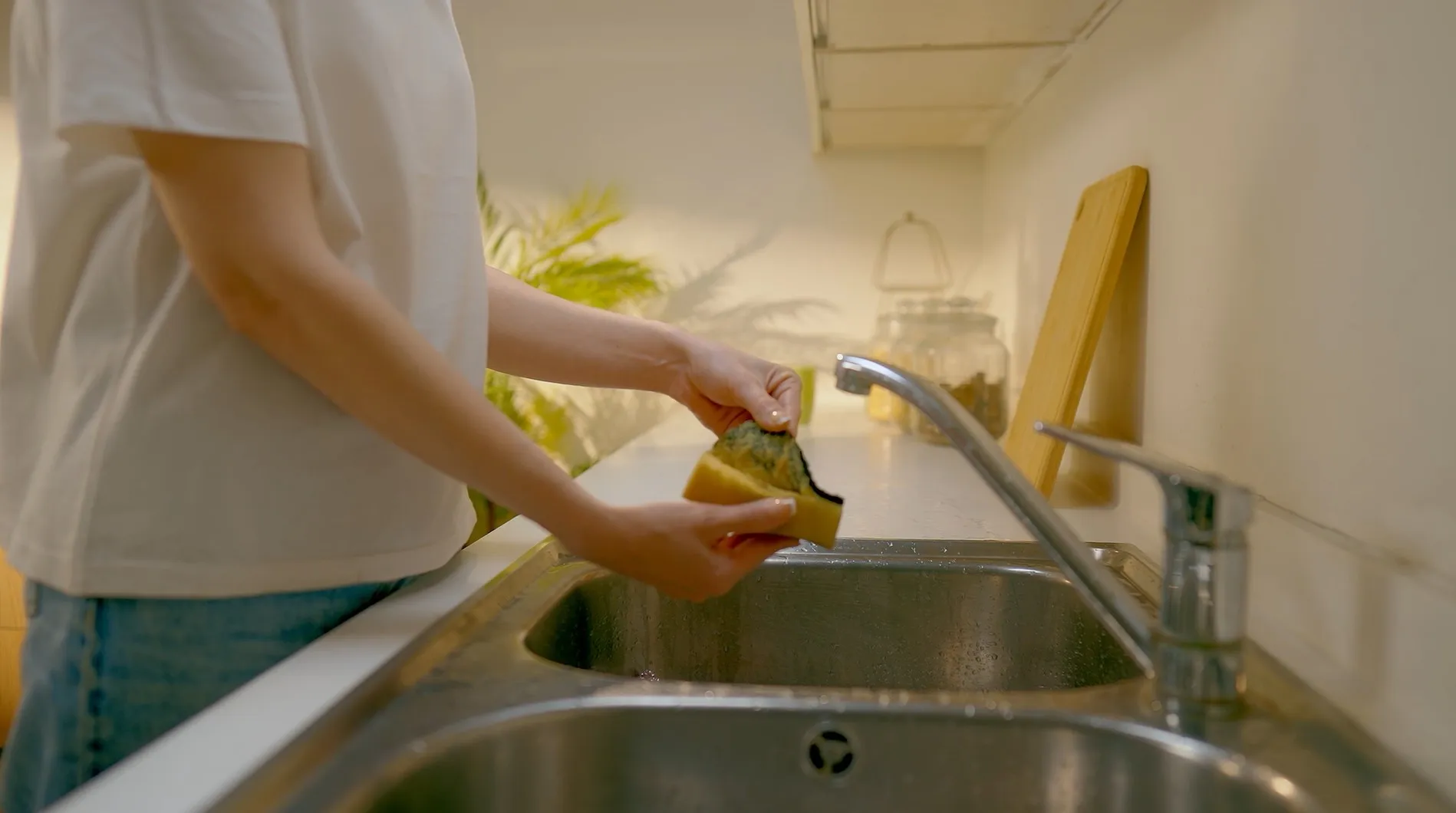 Hands pulling a worn sponge apart over the kitchen sink