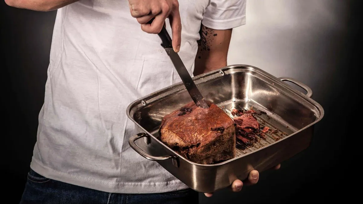guy cutting a fruitcake inside a pan with a knife